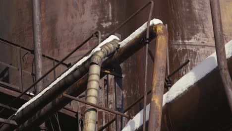 Close-up-of-rusty-industrial-pipes-and-structures,-with-snow-accumulated-on-top-of-them