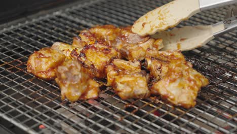Close-up-shot-of-pork-ribs,-meat-grabbed-with-tongs-on-the-grill-by-a-cook
