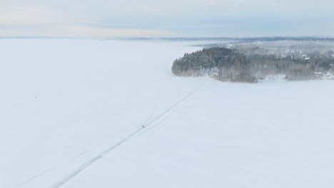 A-couple,-two-people,-walking-on-a-road-or-path-on-ice-towards-a-small-cape-on-a-frozen-lake-in-Tammela,-Finland