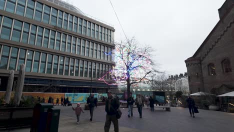 People-Walking-Across-Courtyard-At-Beside-Kings-boulevard-Past-Tree-With-Illuminated-LED-Strips-Along-Tree-Branches