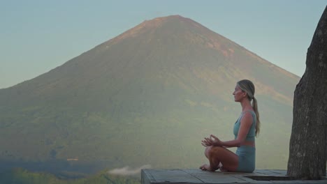 Woman-meditating-in-easy-pose-on-wooden-platform-inhaling-air,-Mount-Agung