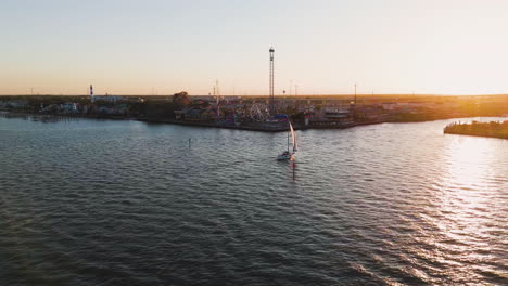 Aerial-view-of-a-boat-sailing-in-front-of-the-Kemah-Boardwalk,-sunset-in-Texas,-USA