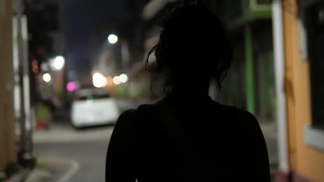 Unrecognizable-young-girl-with-solitude-walking-alone-on-a-dimly-lit-street-at-night
