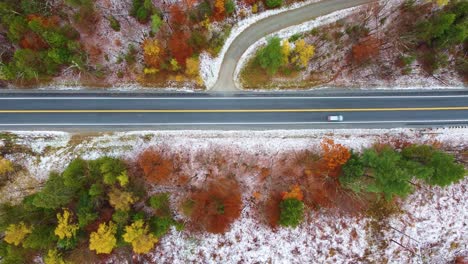 Topdown-view-Along-asphalt-road,-Autumn-colored-trees-and-snow,-New-Hampshire,-USA