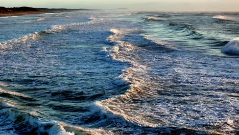Luftaufnahme-Der-Schaumigen-Wellen,-Die-Gegen-Die-Küste-Schlagen,-Und-Das-Sonnenlicht-Wirft-Einen-Goldenen-Schimmer-Auf-Den-Schaum-Des-Ozeans