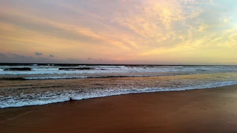 Die-Sanften-Pastelltöne-Der-Morgendämmerung-Spiegeln-Sich-Am-Strand,-Die-Wellen-Streichen-Sanft-über-Den-Sand-Unter-Einem-Wolkenverhangenen-Himmel