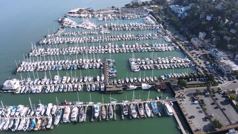 Drone-descends-over-the-marina-in-Sausalito,-showcasing-rows-of-moored-boats-and-the-stunning-coastal-town-near-San-Francisco