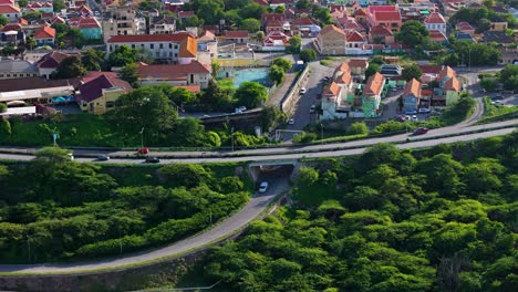 Luftaufnahmen-Etablieren-Eine-Umlaufbahn-Um-Autos,-Die-Unter-Der-Brücke-Mit-Den-Ikonischen-Häusern-Mit-Orangefarbenen-Dächern-Von-Curaçao-Fahren