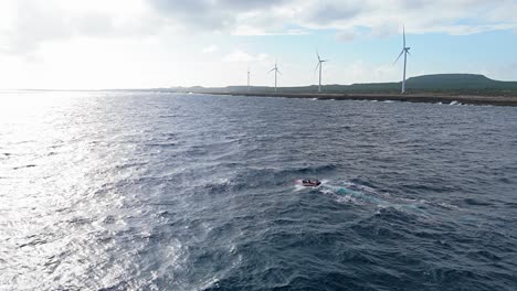Fishermen-brave-rocky-seas-in-small-boat-off-northside-of-playa-kanoa-in-Curacao-with-windmill-turbines
