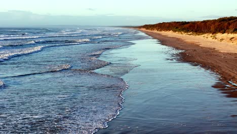 Sanfte-Wellen-Plätschern-An-Der-Sandigen-Küste-Eines-Einsamen-Strandes,-Eine-Ruhige-Küste-Erstreckt-Sich-In-Die-Ferne