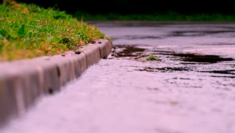 Rainwater-runoff-downhill-towards-concrete-street-drain,-telephoto-shot