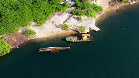 Drone-orbit-around-rusted-sunken-or-abandoned-boat-anchored-off-white-coastal-sandy-beach