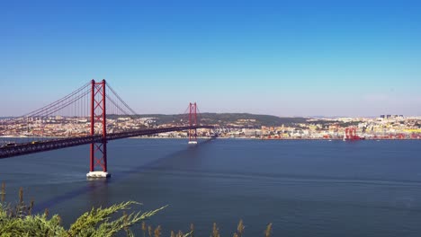 Amazing-architecture-of-the-25-de-Abril-suspension-bridge-and-passing-traffic-at-daytime-with-the-view-of-Lisbon-in-the-background,-Portugal