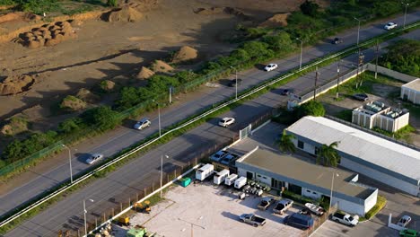 Aerial-parallax-around-cars-driving-on-tropical-highway-next-to-industrial-factory-buildings