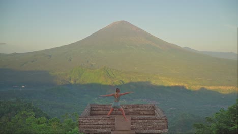 Woman-practicing-fierce-warrior-pose-on-wooden-platform-in-front-of-mount-Agung