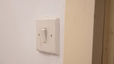 Turning-an-old-worn-light-switch-on-and-off-delicately-with-a-finger,-manipulating-the-aged-mechanism