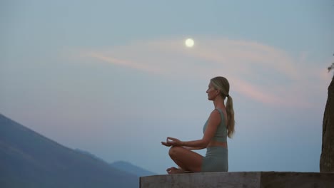 Mujer-Meditando-En-Pose-De-Yoga-Sentada-Sobre-Una-Plataforma-De-Madera-Con-Luna-Llena