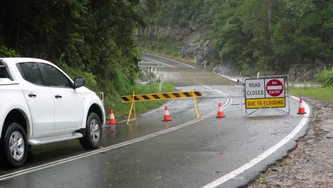 Mudgeeraba,-Gold-Coast-02-January-2024---White-car-waits-at-road-closure-due-to-flooding-across-Mudgeeraba-Creek-Bridge-causing-road-closure