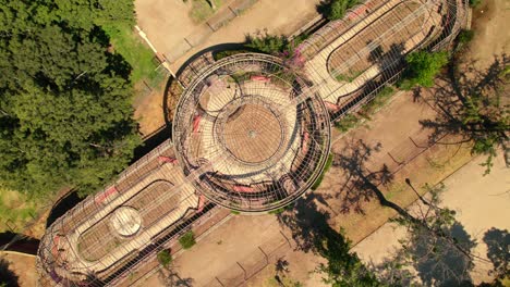 Aerial-Drone-Fly-360-Above-Greenhouse-Metallic-Structure-in-Public-Square-Park,-Green-Trees,-Fence-Architecture,-Invernadero-de-la-Quinta-Norma