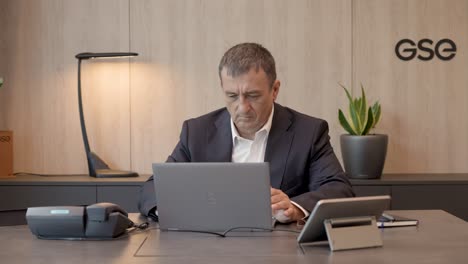 Corporate-manager,-seated-in-modern-office,-using-laptop-on-polished-desk