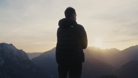 Man-putting-on-his-jacket-during-hike-at-sunset