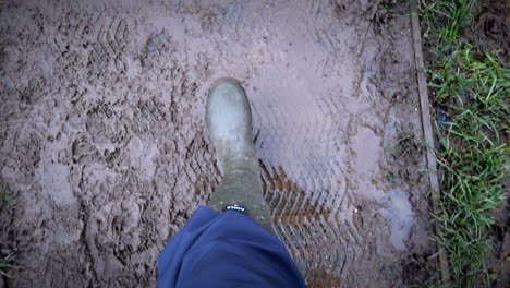 Muddy-conditions-after-heavy-rainfall-as-a-rambler-wearing-wellington-boots-walks-in-the-English-countryside