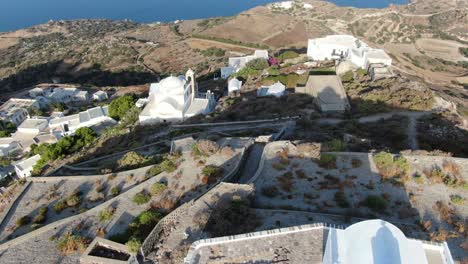 Drohnenansicht-In-Griechenland,-Die-über-Eine-Weiße-Kirche-Auf-Einem-Hügel-Fliegt,-Mit-Einer-Griechischen-Weißen-Hausstadt-Mit-Blick-Auf-Das-Blaue-Meer-Auf-Einem-Berg