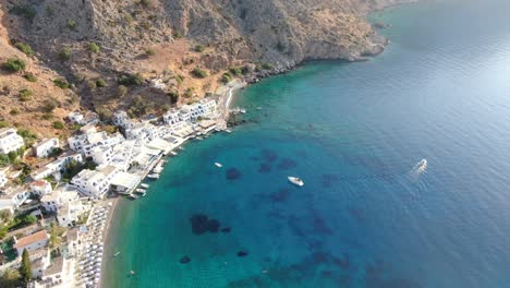 Vista-De-Drones-En-Grecia-Volando-Sobre-El-Mar-Azul-En-Loutro,-Pequeña-Ciudad-De-La-Casa-Blanca-Y-Pequeños-Barcos-Junto-A-Una-Colina-En-Un-Día-Soleado