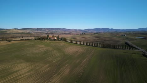 Mowed-rows-of-grass-sit-below-mansion-in-Val-d'Orcia-Tuscany-with-epic-road-leading-up-to-villa