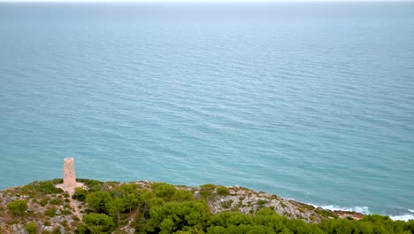 Horizontal-4K-time-lapse-of-the-Mediterranean-Sea-waves-calmly-arriving-at-the-coastline-by-a-defensive-medieval-stone-tower-in-Oropesa-del-Mar,-Spain