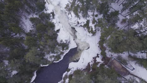 Aerial-drone-shot-captures-the-breathtaking-beauty-of-a-frozen-waterfall-nestled-in-a-wintry-forest-landscape