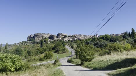 Landscape-with-a-road-through-nature-leading-to-a-small-historic-stone-village-in-strong-sun