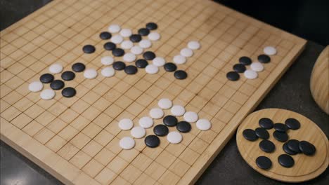 45-degree-overhead-angle-of-hand-playing-white-stone-in-Go-board-game-with-tiles-already-on-grid-and-black-pieces-in-corner