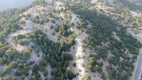 Vista-De-Drones-En-Grecia-Volando-Sobre-Una-Montaña-Marrón-Y-Verde-Con-Camino-Serpenteante-Y-Mar-En-El-Horizonte-En-Un-Día-Soleado