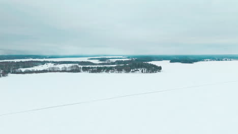 Flying-over-a-road-on-frozen-lake-ice-to-reveal-a-landscape-of-a-snowy-forest