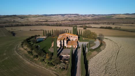 Orange-roof-historic-stone-mansion-overlooks-pond-and-fields-in-Val-d'Orcia-Tuscany
