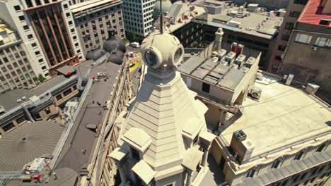 Aerial-360-Drone-Around-Iconic-Roofs-and-Tower-Cusp-in-Ariztia-Building-at-Chile,-La-Bolsa-Neighborhood,-Santiago-Cityscape-in-Summer