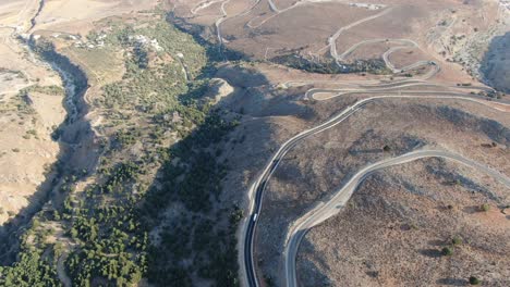 Drone-view-in-Greece-flying-over-a-brown-and-green-mountain-with-serpent-road-and-sea-on-the-horizon-on-a-sunny-day