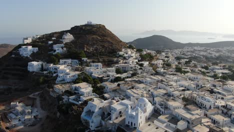 Drone-view-in-Greece-circling-in-front-of-greek-town-with-white-houses-on-a-brown-hill-and-sea-on-the-horizon-on-a-sunny-day