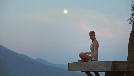 Woman-on-wooden-platform-grabbing-notebook-to-write-down-feelings-during-full-moon