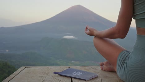 Notebook-beside-woman-in-yoga-pose-meditating-in-front-of-volcano,-Journaling-concept