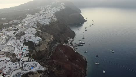 Drohnenansicht-In-Griechenland,-Die-Bei-Sonnenaufgang-über-Santorini-Mit-Weißen-Häusern-Der-Stadt-Oia-Auf-Einer-Klippe-Am-Mittelmeer-Fliegt