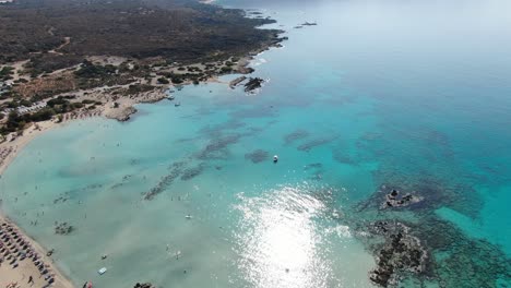 Drone-view-in-Greece-flying-over-Elafonisi-white-sand-narrow-beach,-clear-blue-water-on-the-sides-and-many-umbrellas-on-a-sunny-day