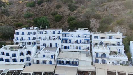 Drone-view-in-Greece-flying-in-front-of-white-houses-next-to-a-brown-hill-on-the-mediterranean-on-a-sunny-day