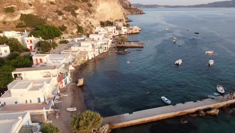 Drone-view-in-Greece-flying-over-a-small-town-with-white-houses-and-colored-doors-next-to-the-sea-and-the-mountain-in-Milos-at-sunset