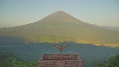 Fit-woman-practicing-yoga-tree-pose-at-Lahangan-Sweet-wooden-platform,-Mount-Agung