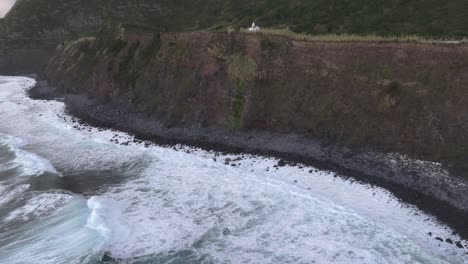 Reveal-shot-of-rugged-cliff-with-church-at-Flores-island,-Aerial