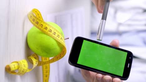 Vertikales-Video-Eines-Ernährungsberaters-Zeigt-Auf-Ein-Smartphone-Mit-Grünem-Bildschirm,-Gesunde-Ernährung