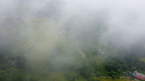 Aerial-flight-through-dense-clouds-showing-idyllic-asian-village-on-slope-in-Nepal