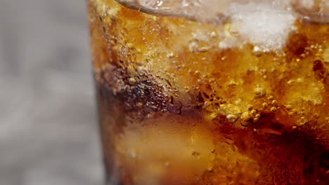 Close-up-shot-of-a-brown-soft-drink-with-ice-in-a-bubbling-glass